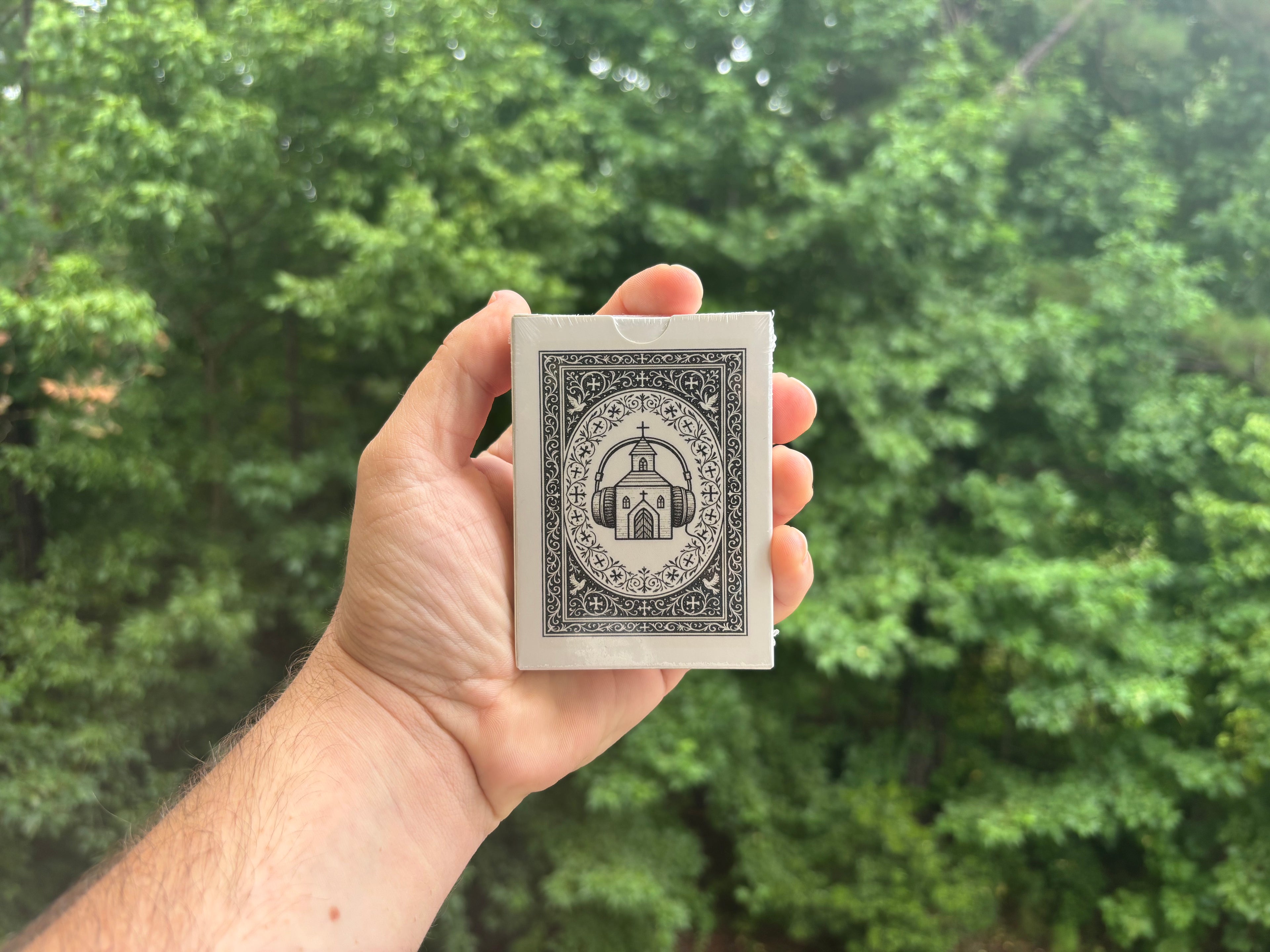Hand holding a deck of playing cards with a church design against a green leafy background